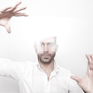 White man with beard and wearing white shirt looking through perspex glass held between his hands