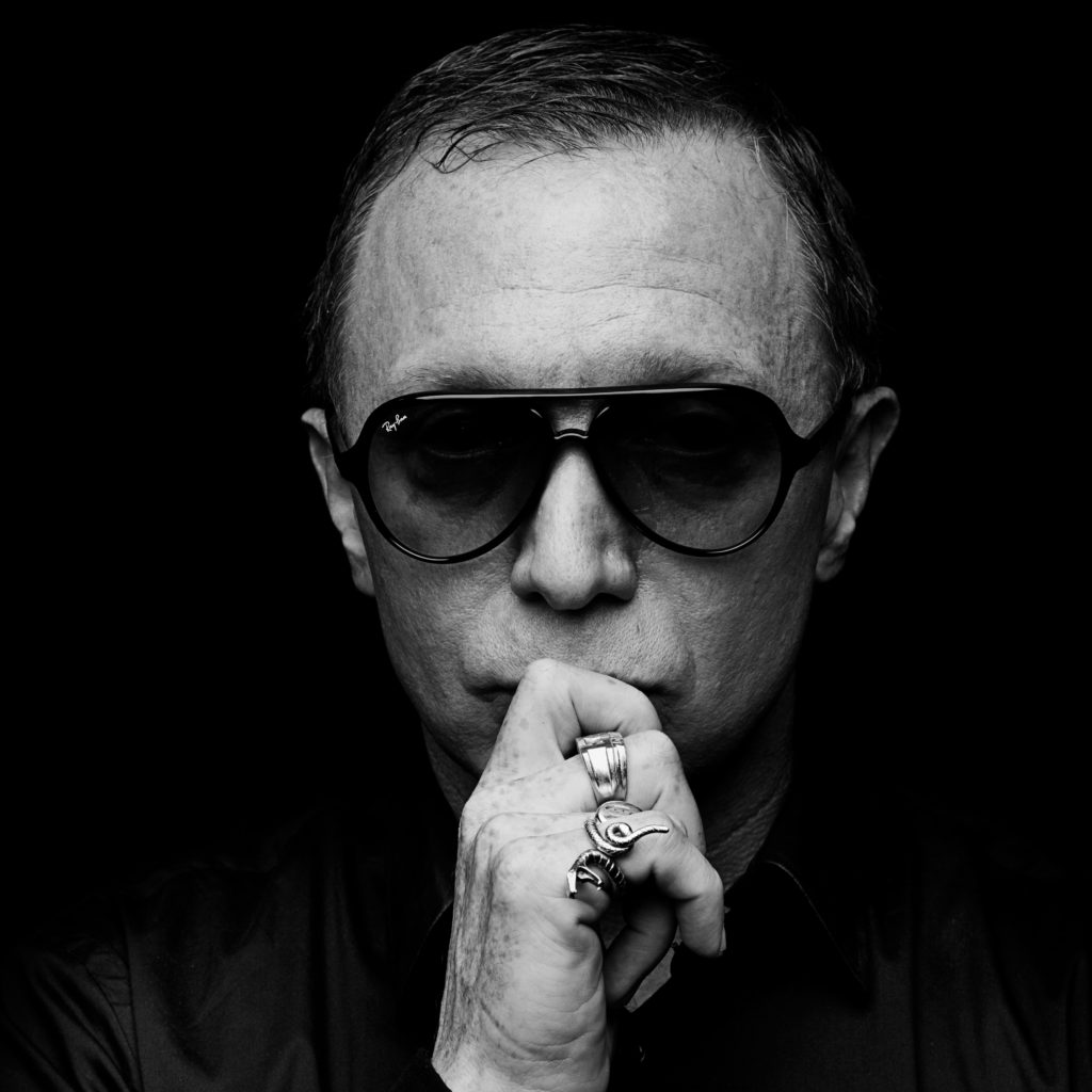 Portrait of Bruce LaBruce with hand covering mouth and dark sunglasses. black and white image