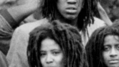 Three black people with dreadlocks, all of their faces partically cut off by the framing in a black and white image.