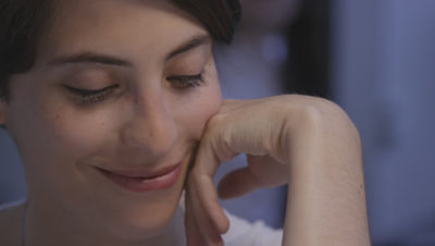 Close up of a white person with short dark hair and lipstick, smiling with their head resting on their hand.