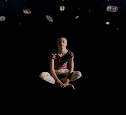 A white boy sitting and floating in black with screens floating above his head.