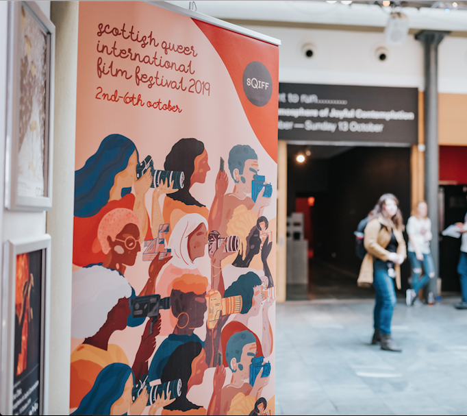 A pop-up banner in an arts centre has 'SQIFF' written on it and an illustration of different, colourful women in rows all holding a different type of camera.