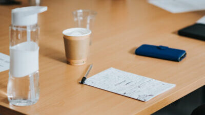 A piece of paper with lots of notes on it sits on a wooden table top alongside a pen, phone, and empty coffee cup.