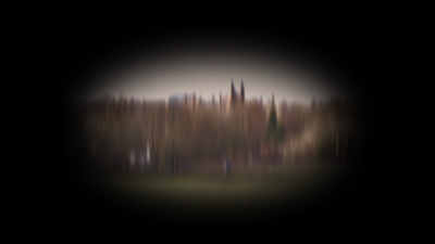 A blurred image of a park with people walking in it and trees and buildings in the background. The image is circular, surrounded by black.