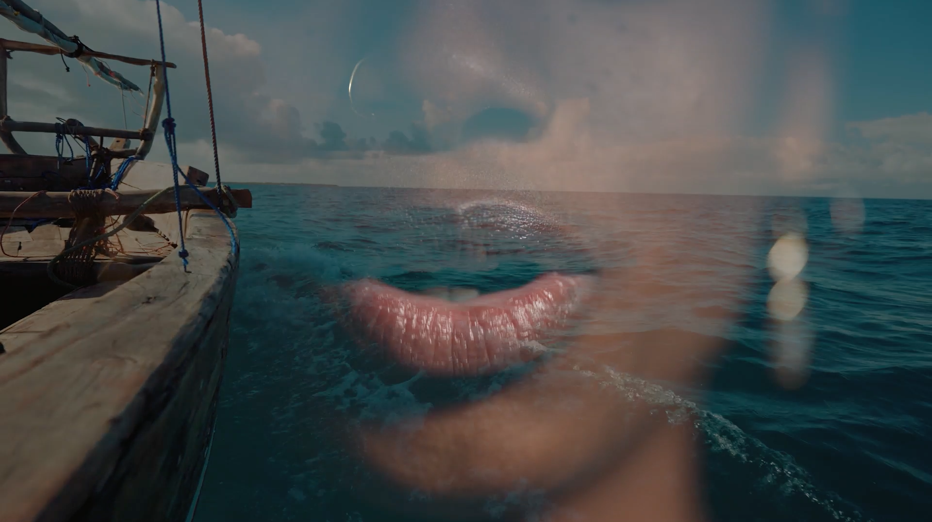 " A non binary Black African person’s mouth slightly open. This is overlayed over the prow of wooden over a turquoise ocean and blue sky on the horizon"