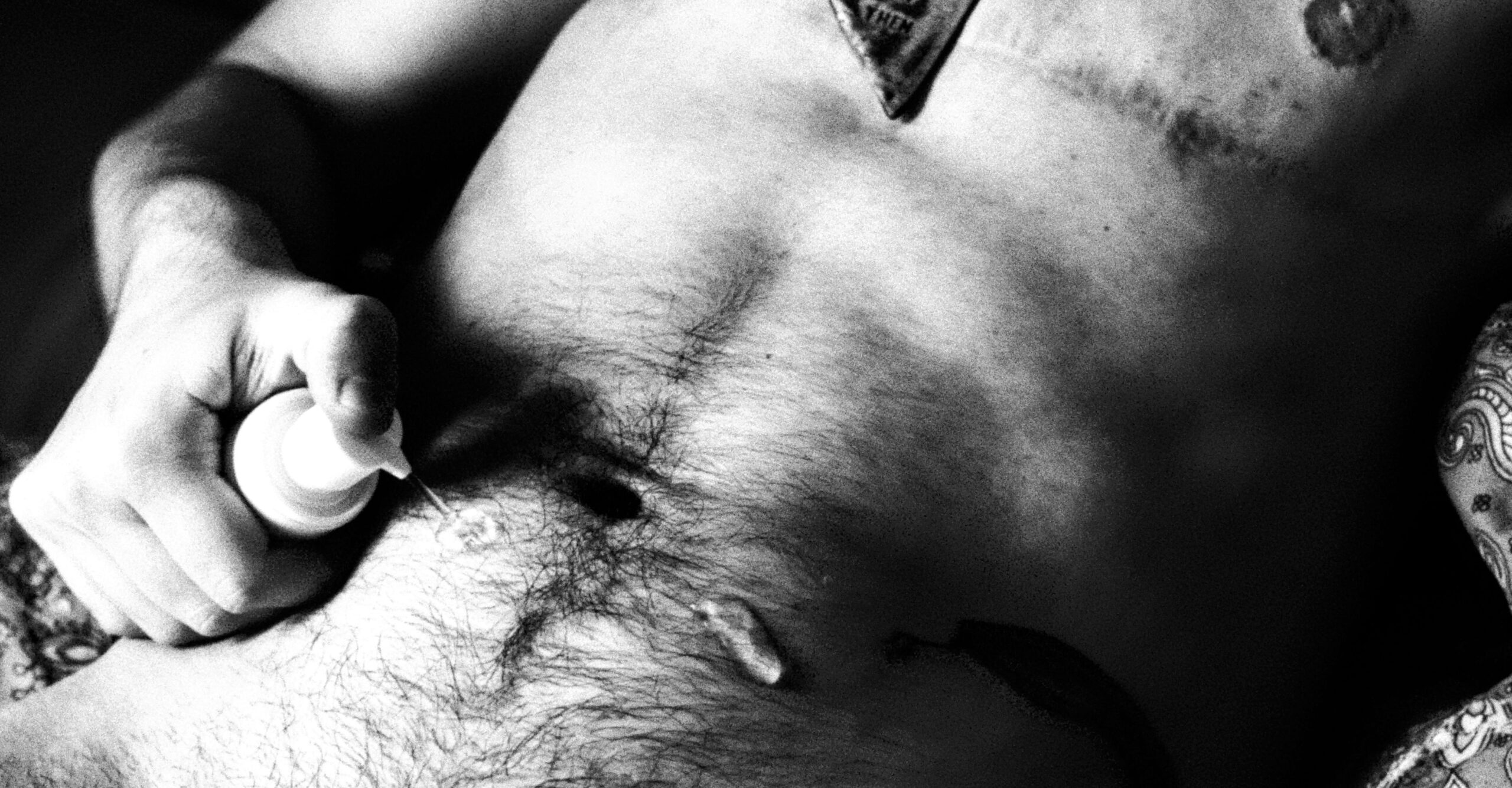 Torso of a trans masculine person applying T-gel on their hairy belly.