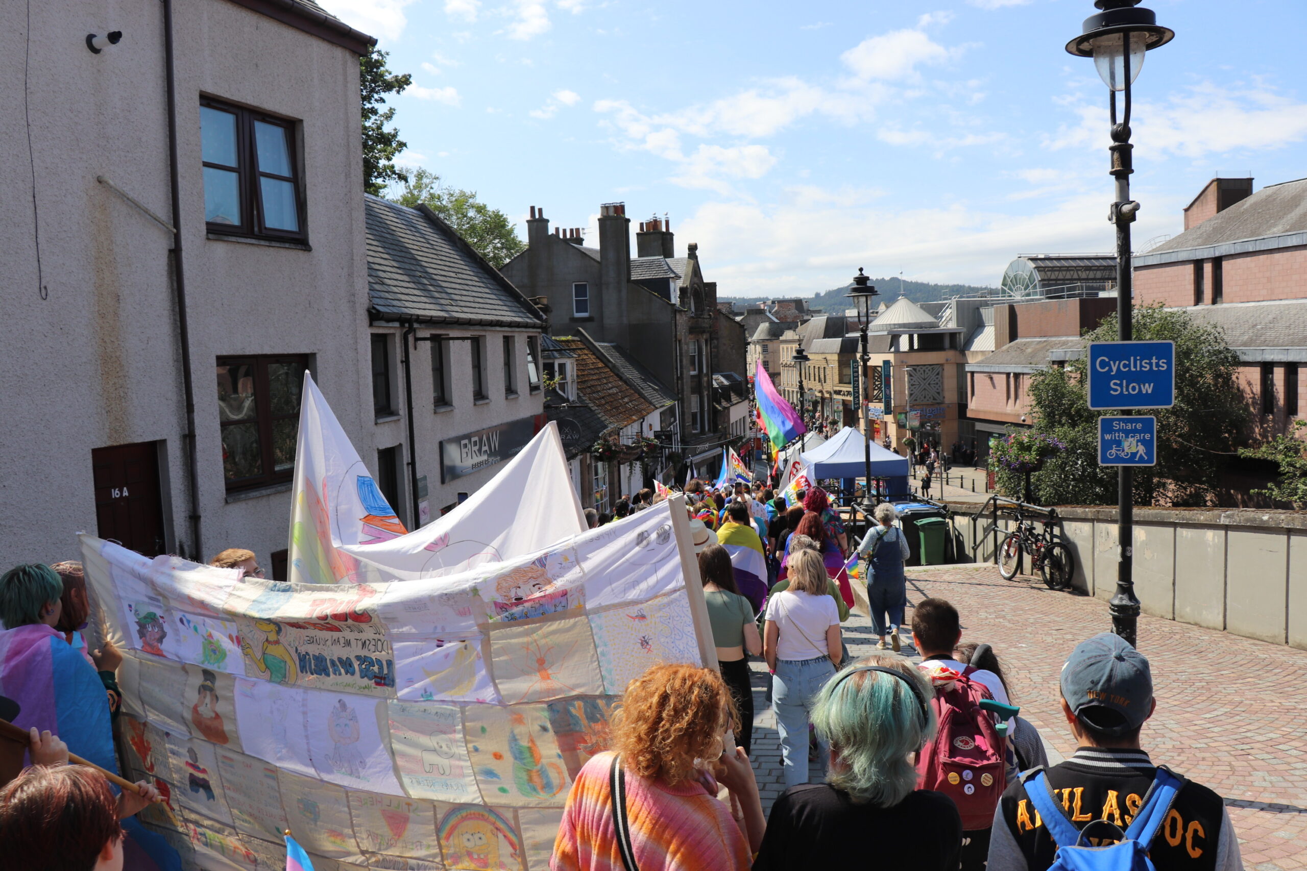 Crowded street at Highland Pride featuring the Queer Youth Arts Collective members and their artwork.