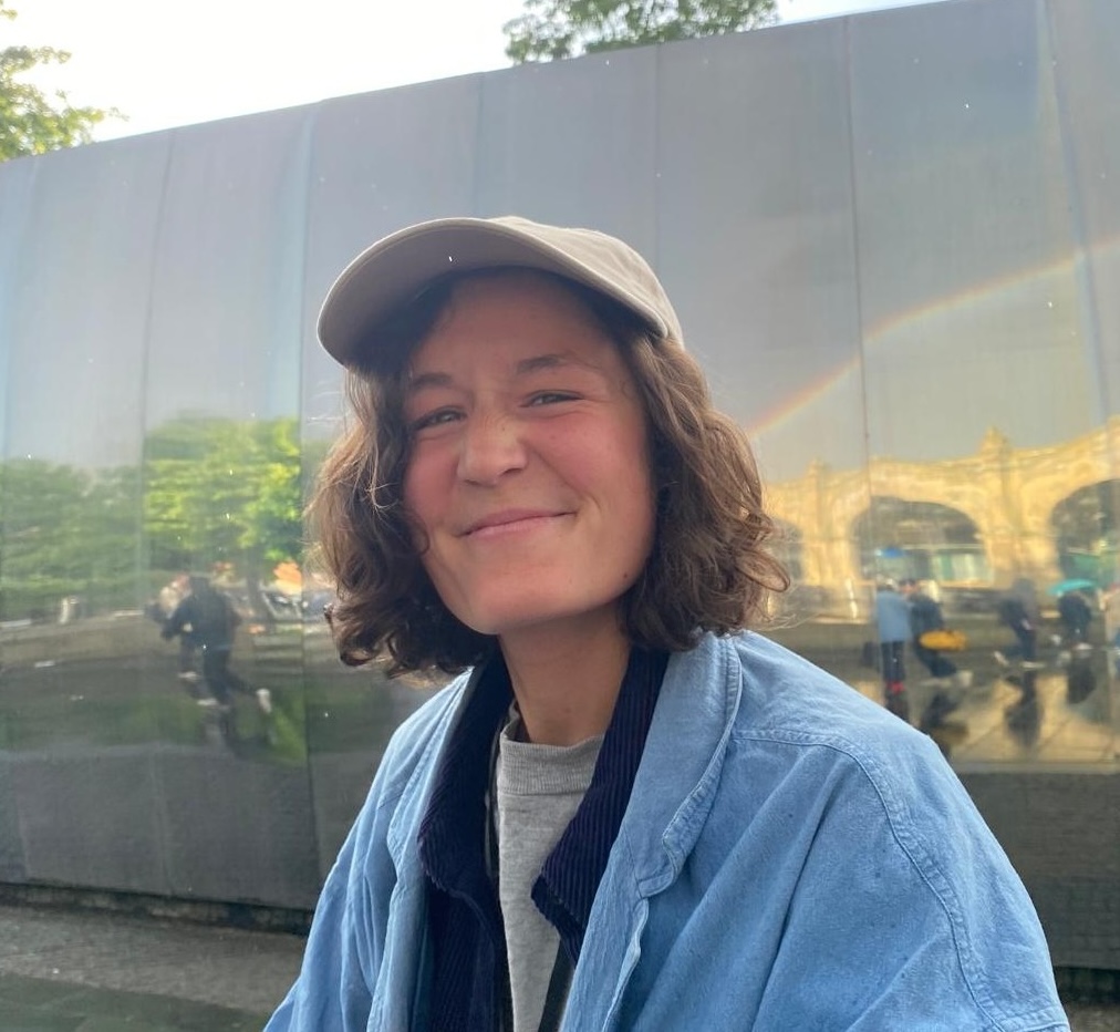 Person with short brown hair wearing a cap and smiling