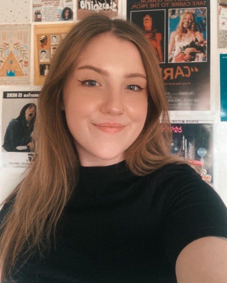 Woman smiling standing against wall filled with film posters
