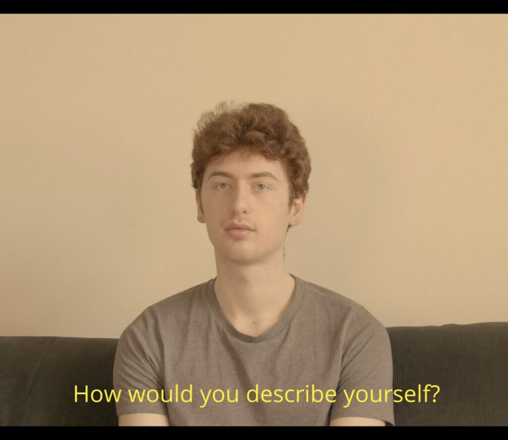 Mid 20s man with red hair and a neutral expression, wearing grey shirt