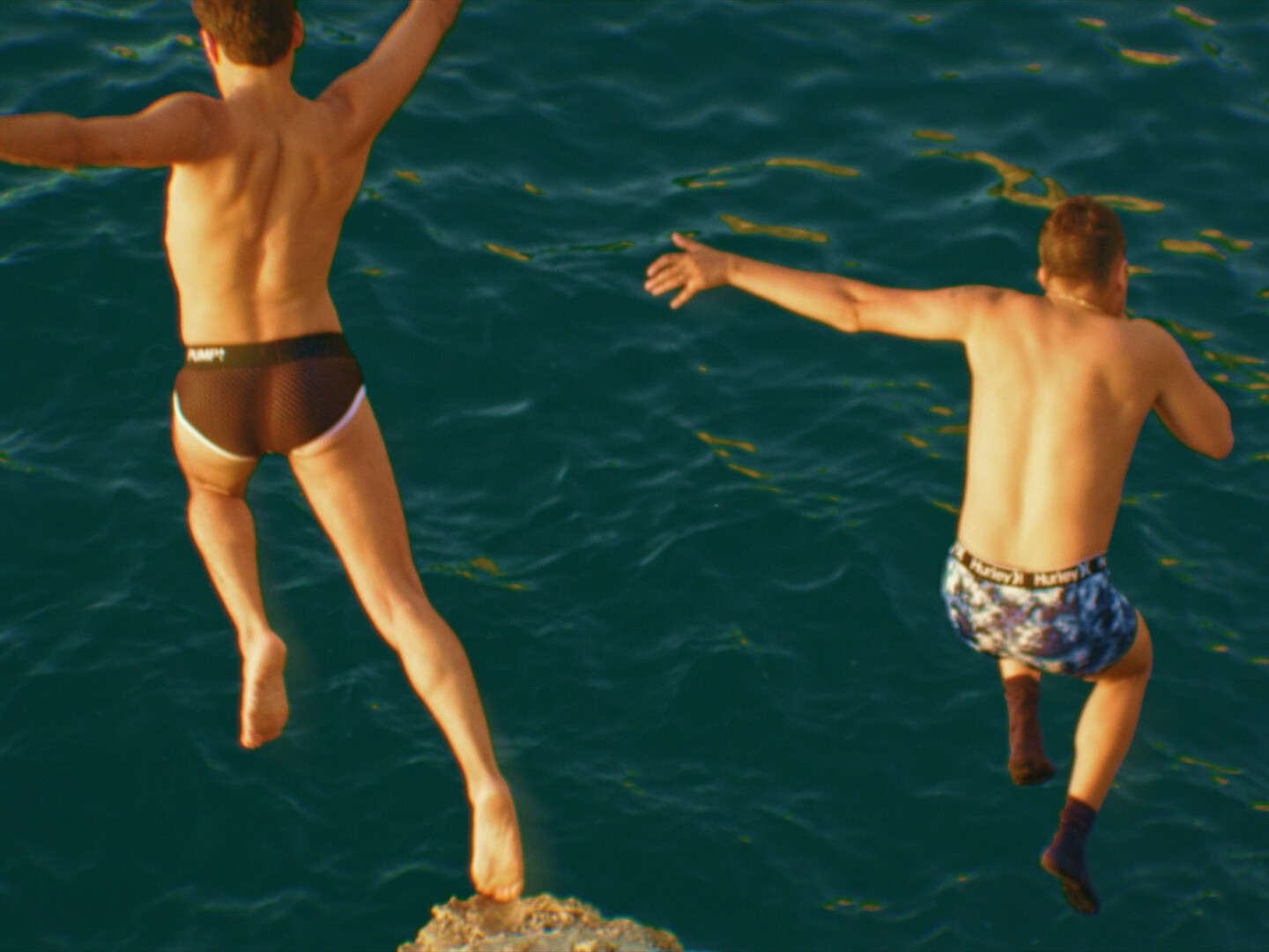 Two guys jumping in the ocean.