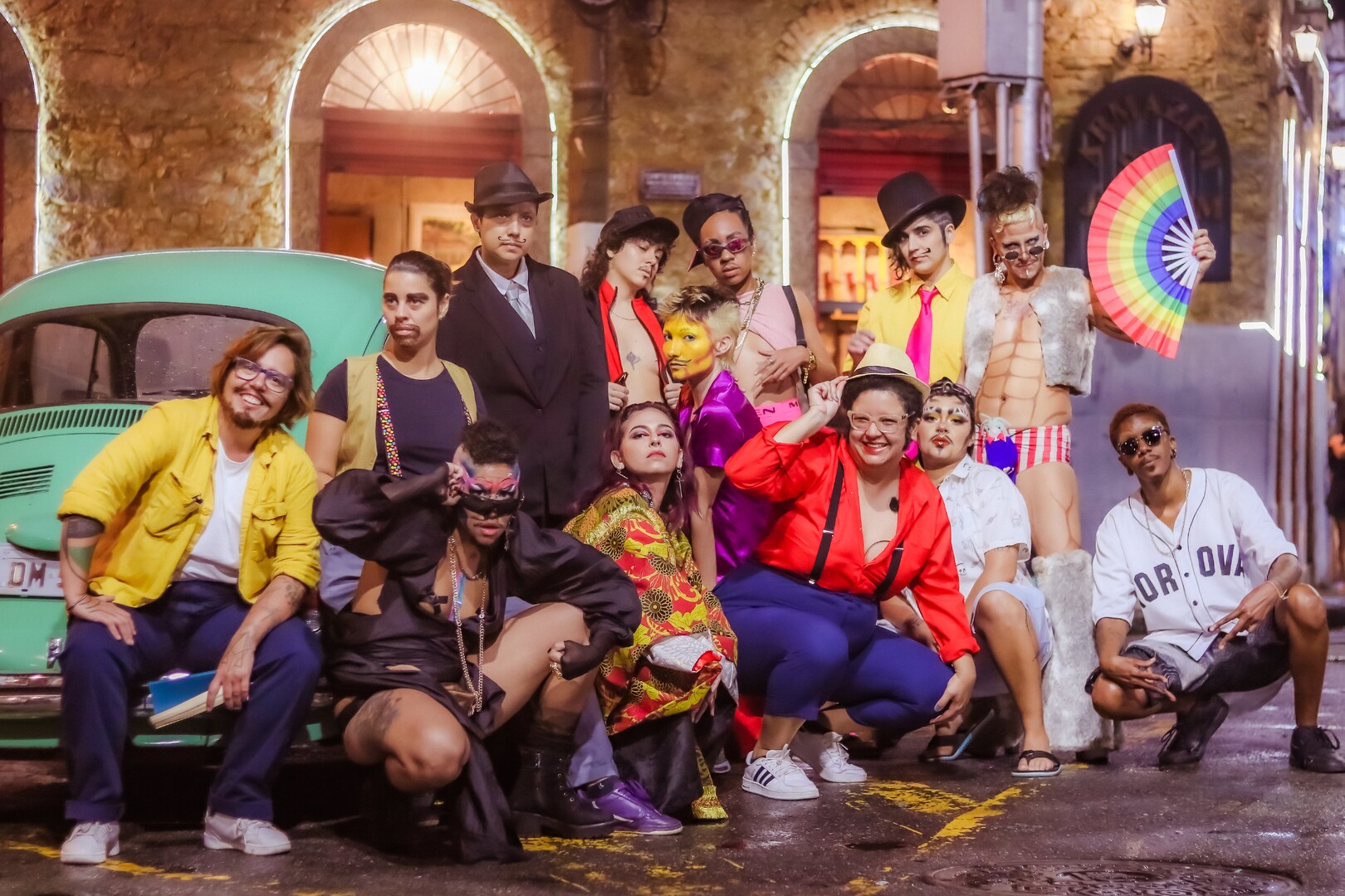 Various drag kings with colourful outfits posing in front of a building.
