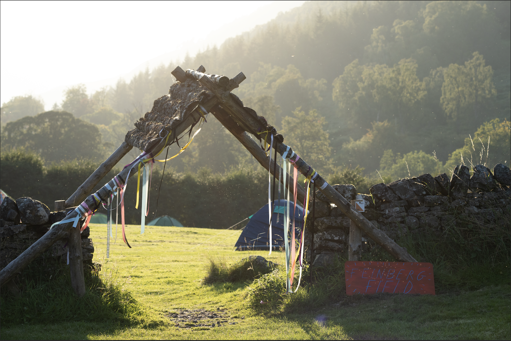 Wooden entrance to campsite with colourful fringing underneath a luscious mountain scenery.