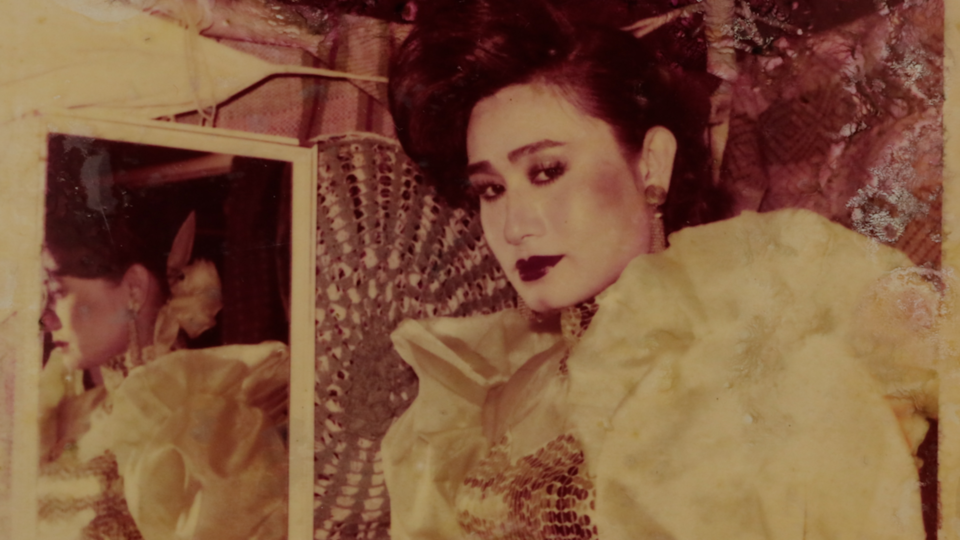 An asian woman in a dressing room wearing makeup looks directly into the camera.