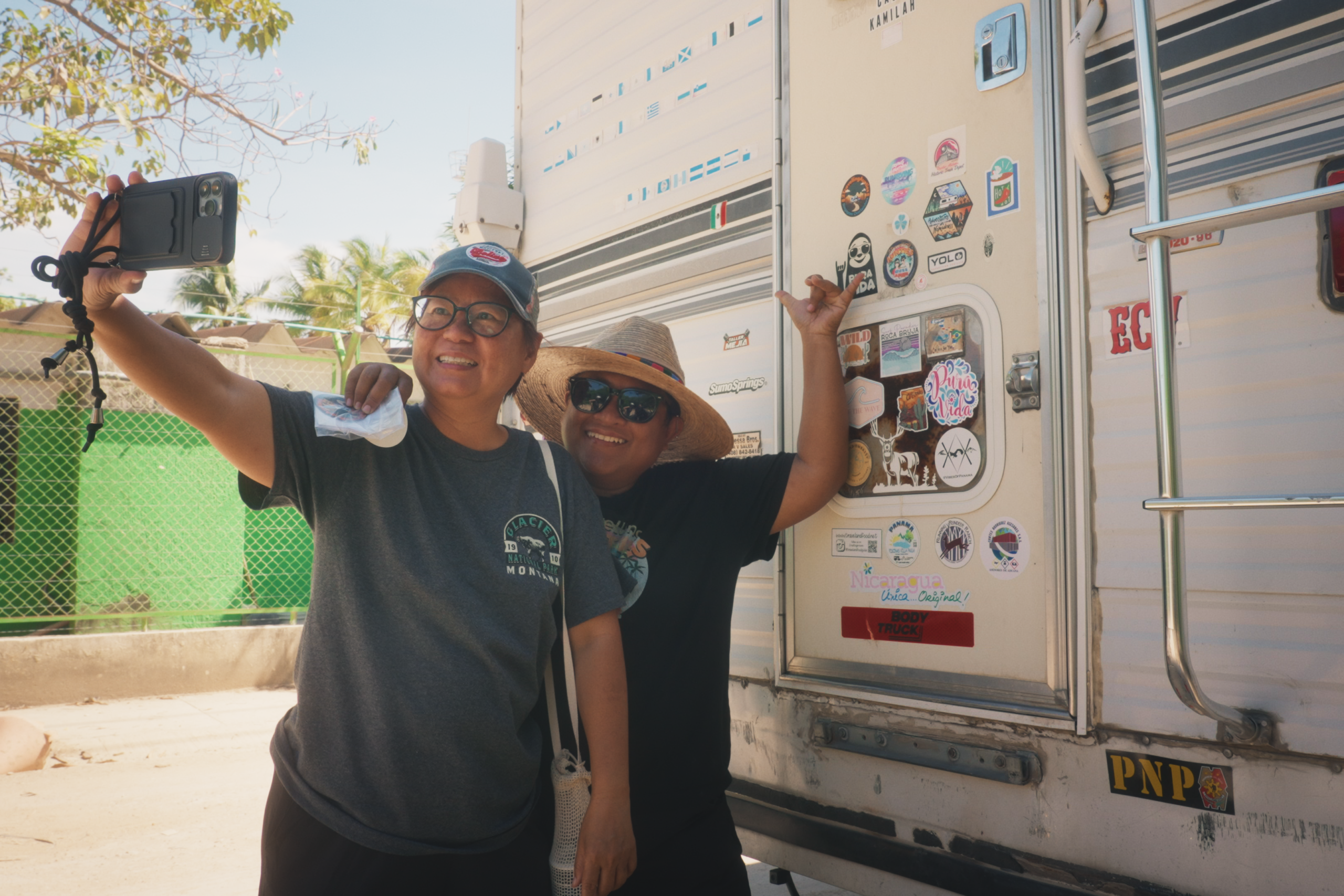 Two aunties smile as they capture a selfie stood next to a stickered camper van.