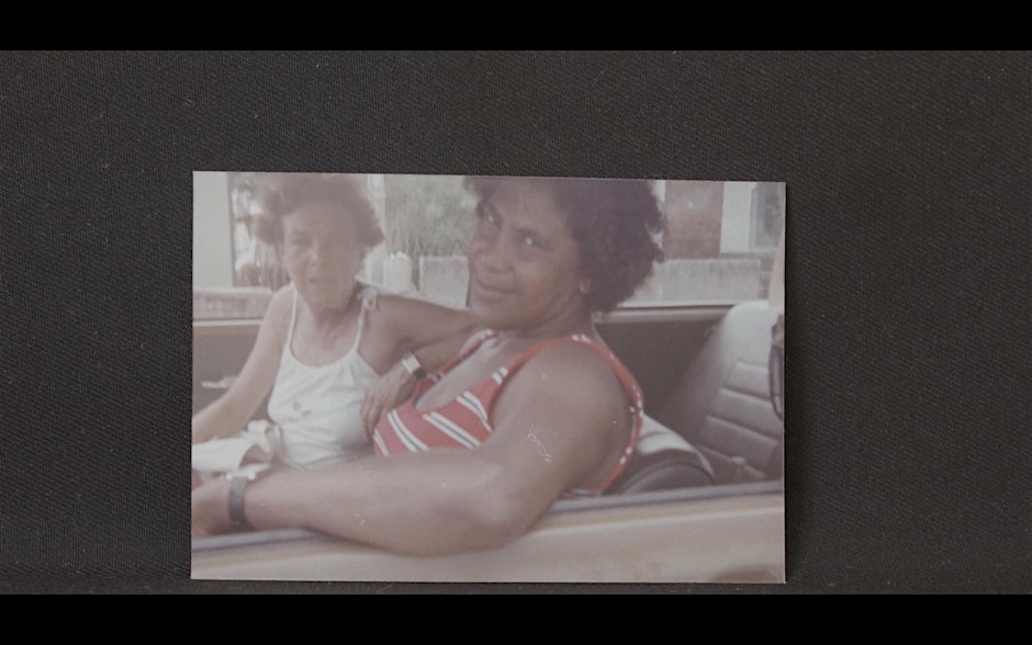 An old photo of two people seating in a vintage car.