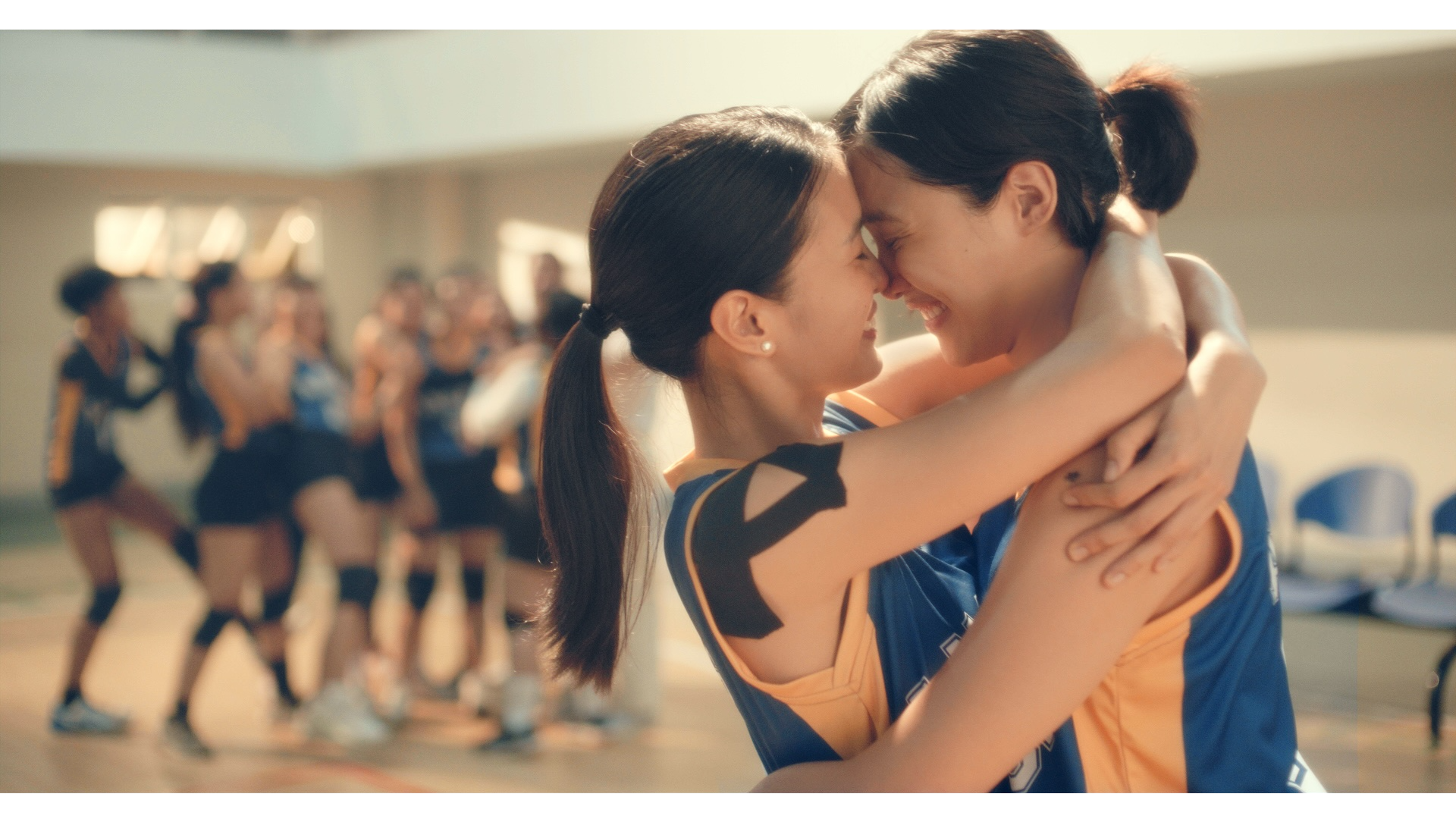 Two asian girls embrace each other in front of their volleyball team.