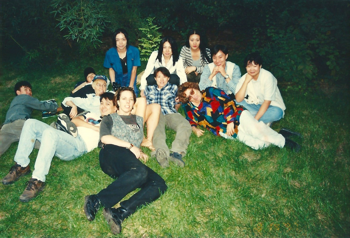 12 people are gathered on the grass of a park in a polaroid-style image