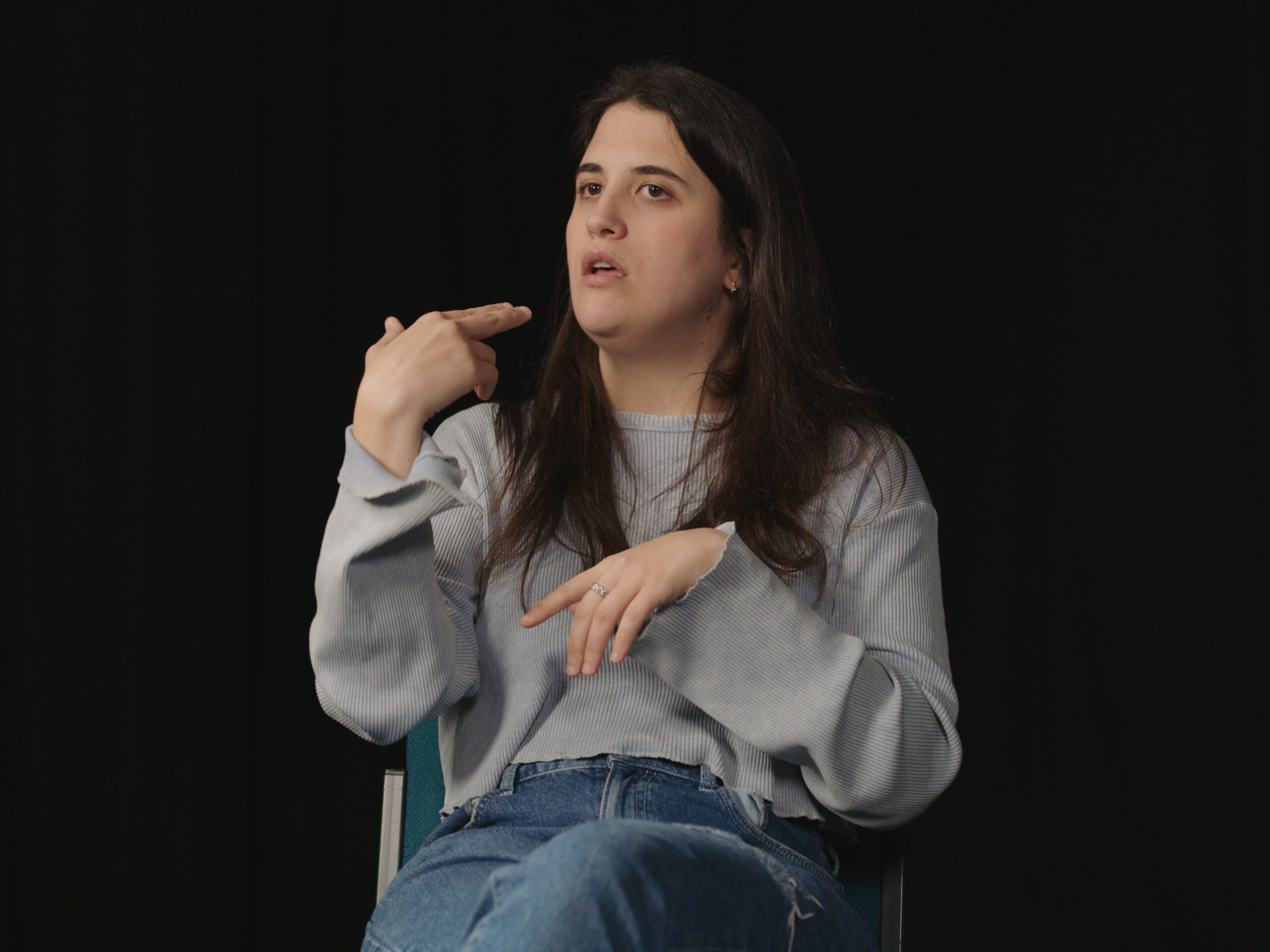 Film's protagonist captured signing mid-conversation while sitting on a chair in front of a black backdrop.