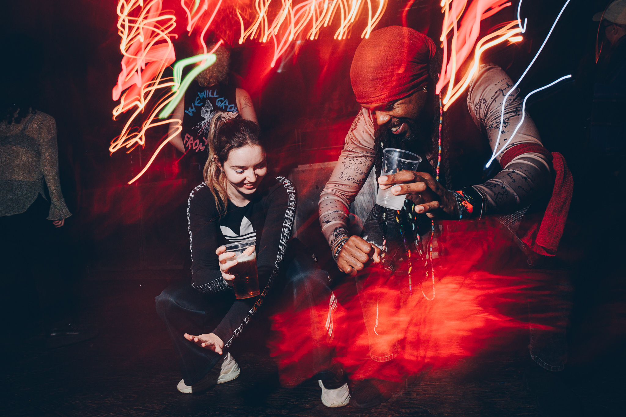 Two people dancing at a party, one is holding a plastic cup. Neon lights shine around them.