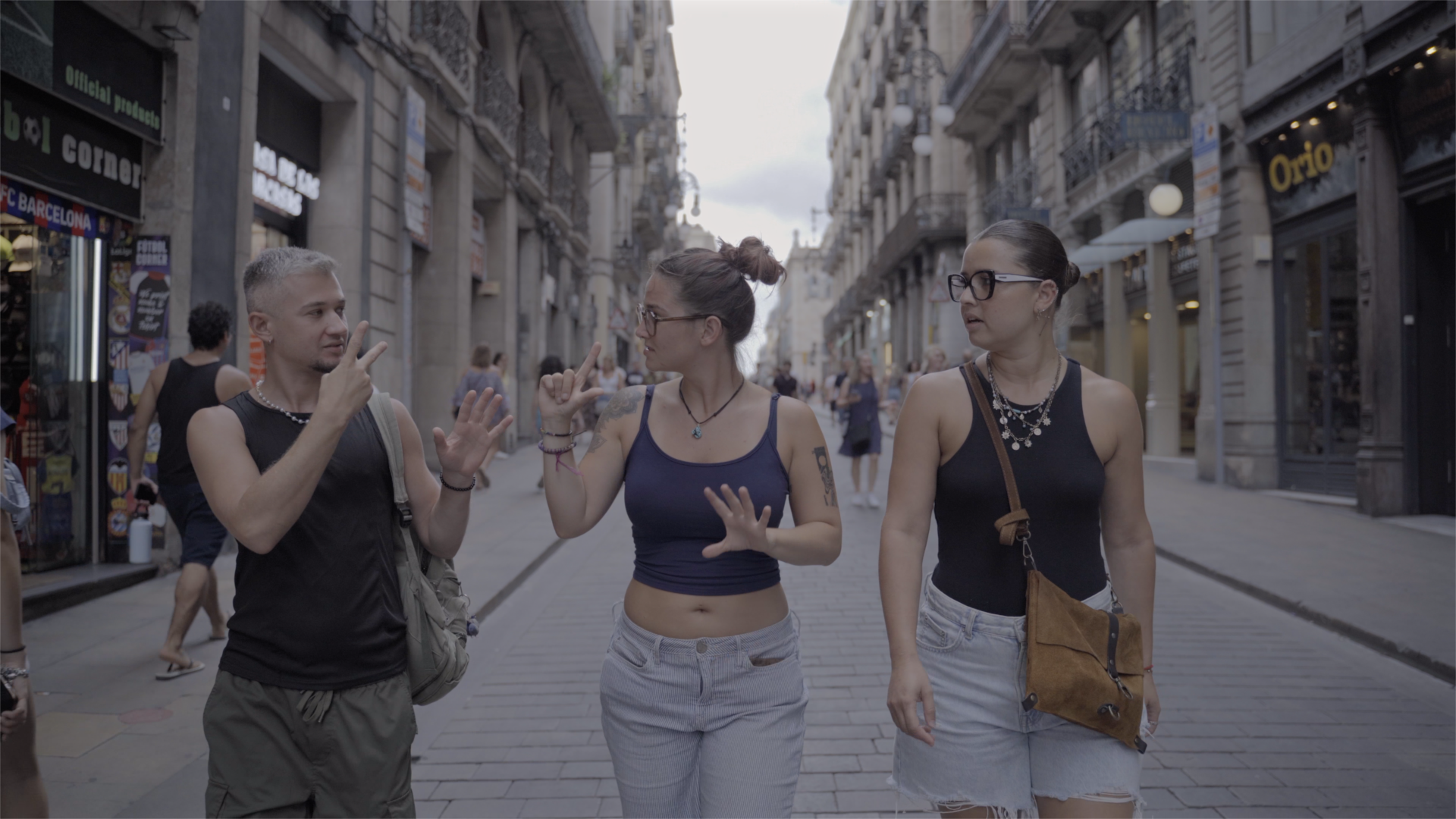 Serhii walking down a busy street in Barcelona with two of his friends, communicating in sign language with the friend beside him as the other friend looks towards them.
