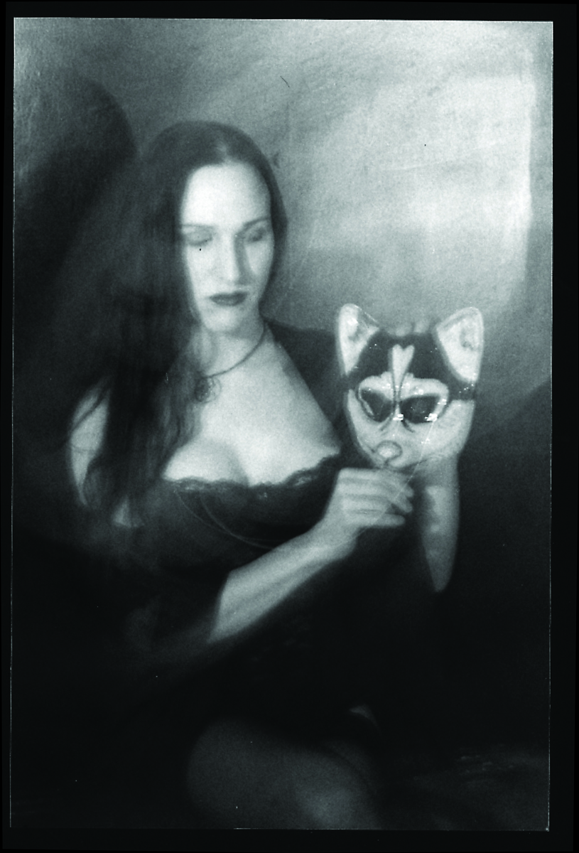 A black and white image of Mirha-Soleil Ross, a white trans woman with long straight hair, holding a fox mask.